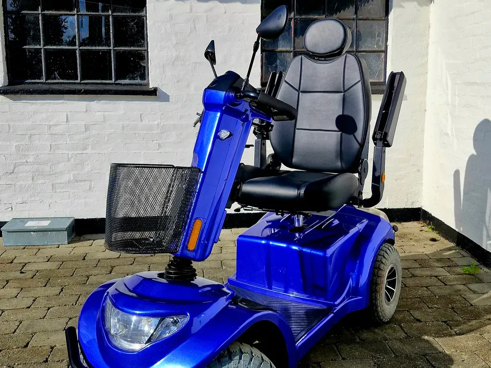 Blå firehjulet elscooter med kurv på en flisebelagt gårdsplads – handicapscooter