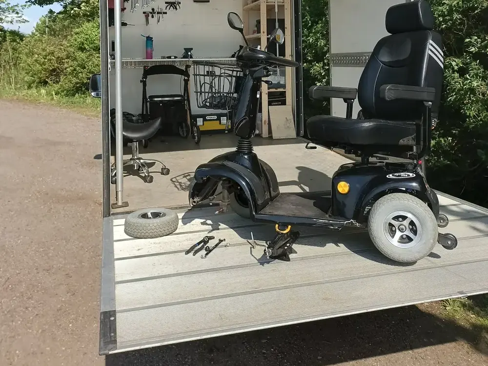 Elscooter på rampen foran værkstedsbilen med et afmonteret hjul og værktøj ved siden af – handicapscooter